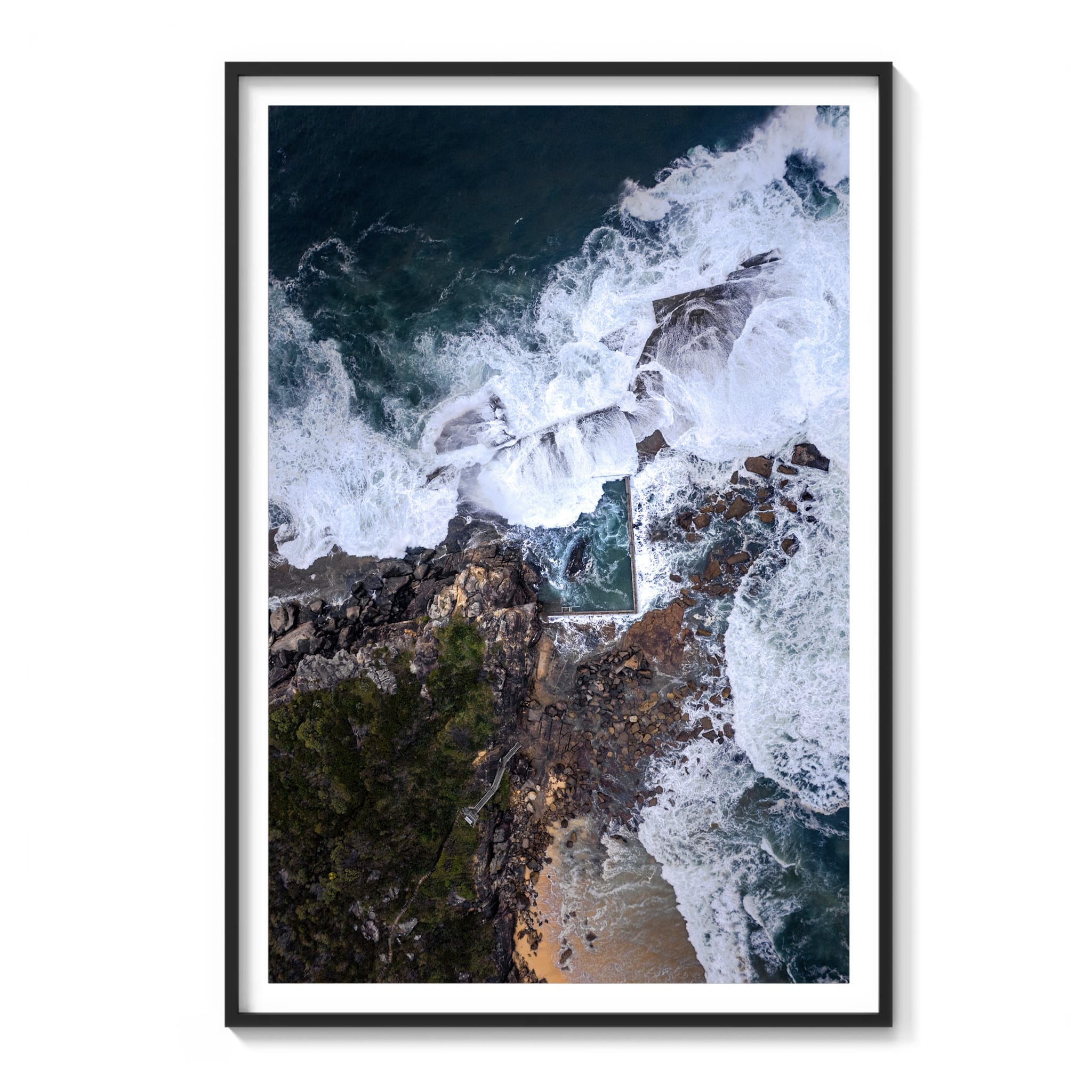 Framed aerial view of waves crashing against rocky cliffs with a small pool below.
