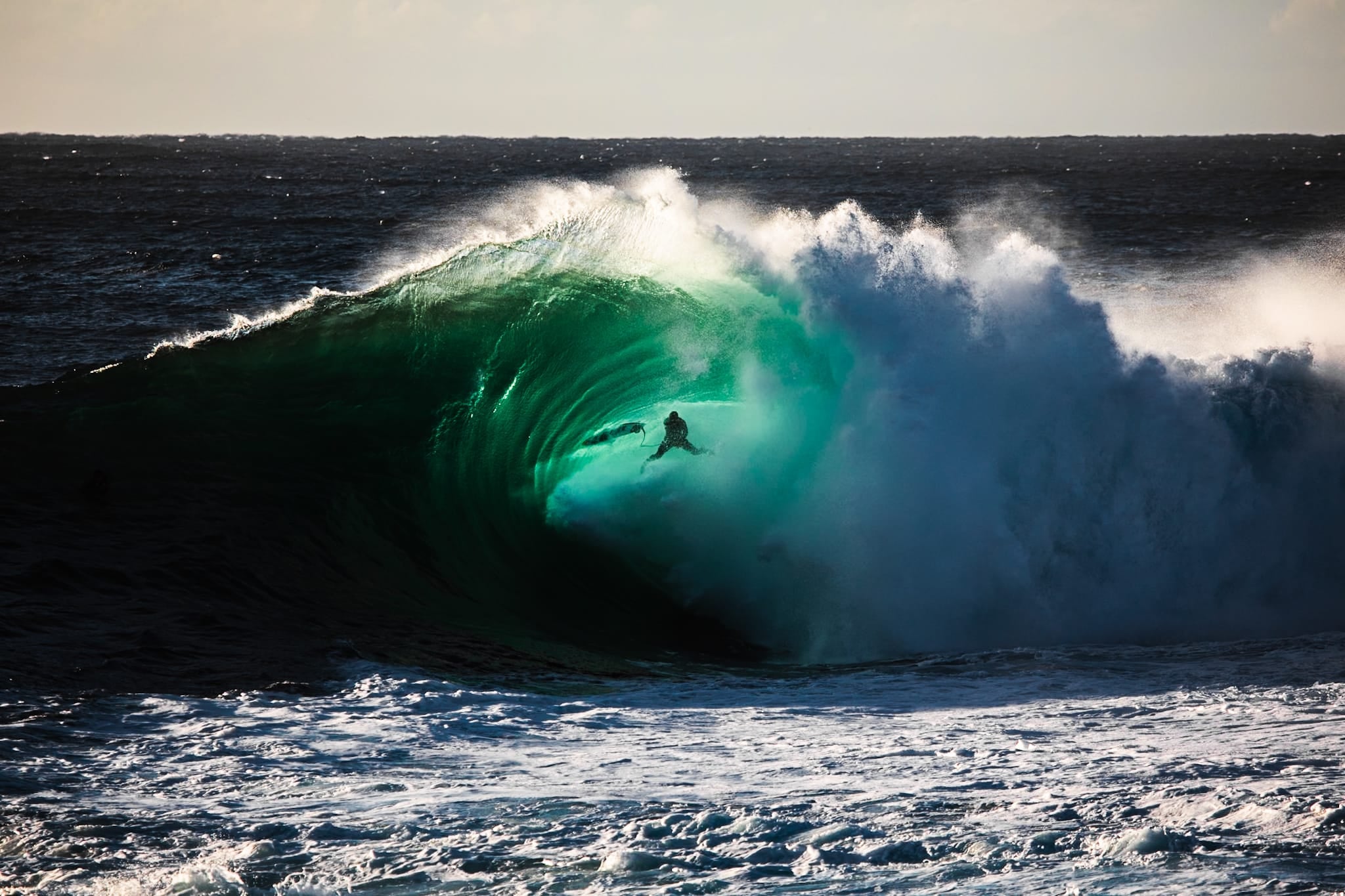 Color photograph of a surfer riding deep inside a dark green barrel wave at Cape Solander.