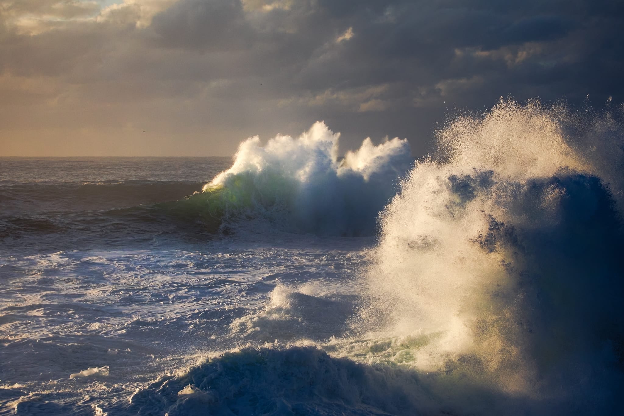 Color photograph of a large breaking wave with green translucent light under stormy skies on the east coast of Australia.