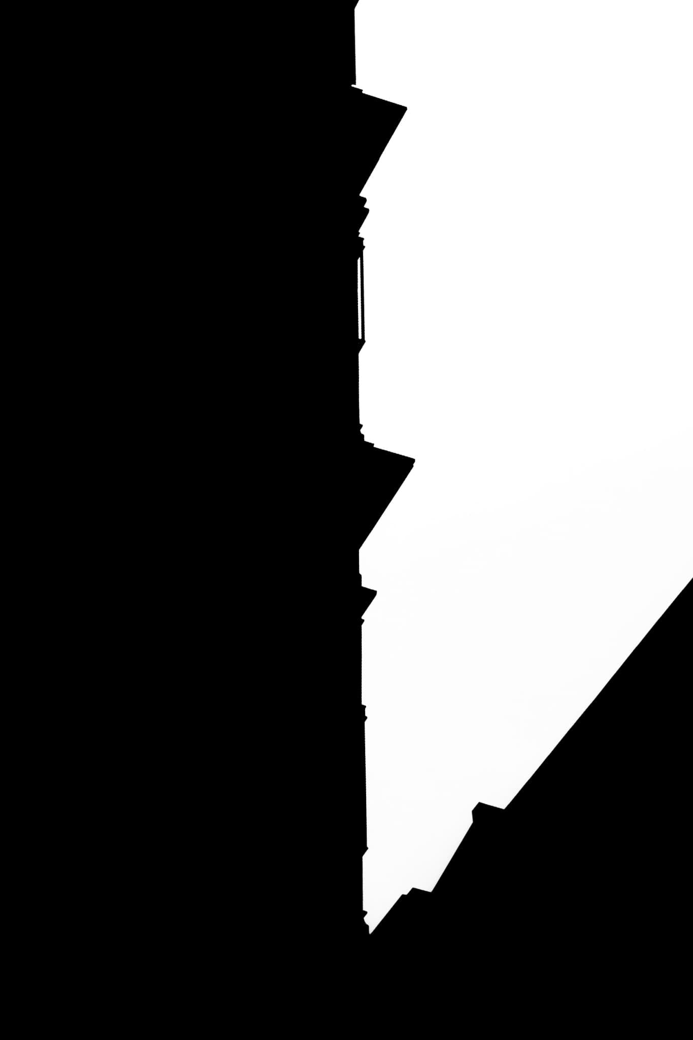 High-contrast black and white photograph of a jagged rooftop silhouette against a bright sky in New York City.