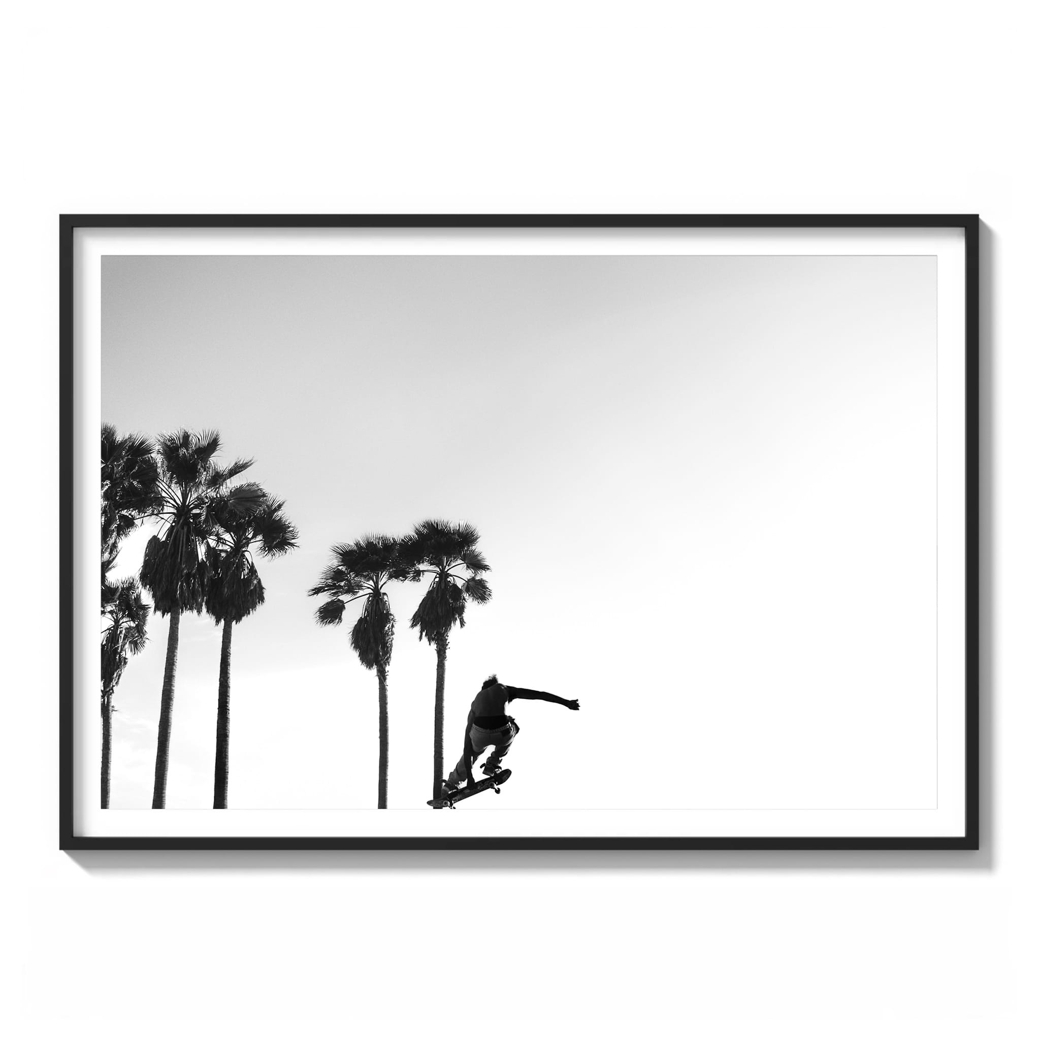 Framed black and white photograph of a skateboarder jumping against an empty sky with palm trees at Venice Beach.