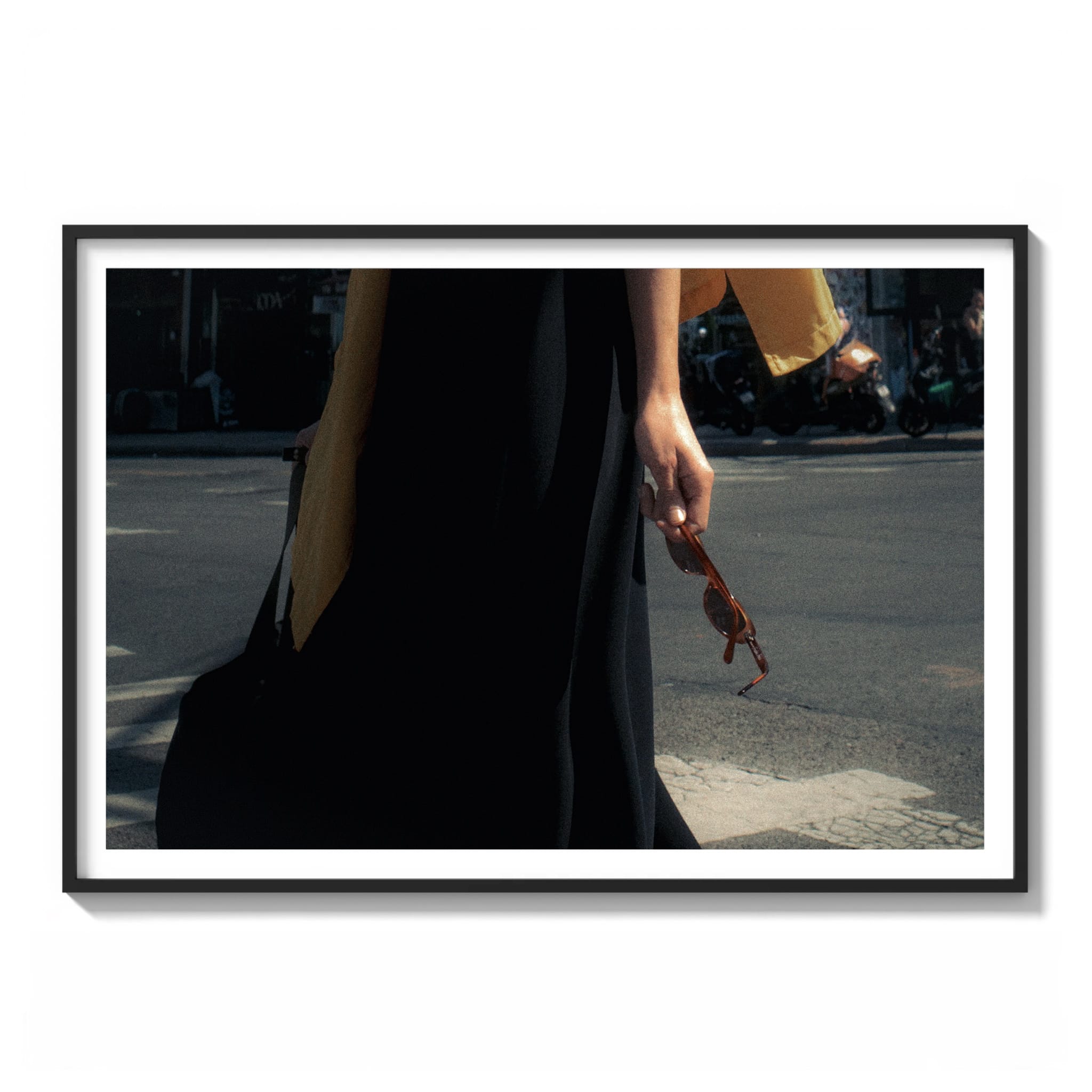 Framed color street photograph of a person in a black dress and mustard scarf holding sunglasses while crossing a street in Brooklyn, New York.