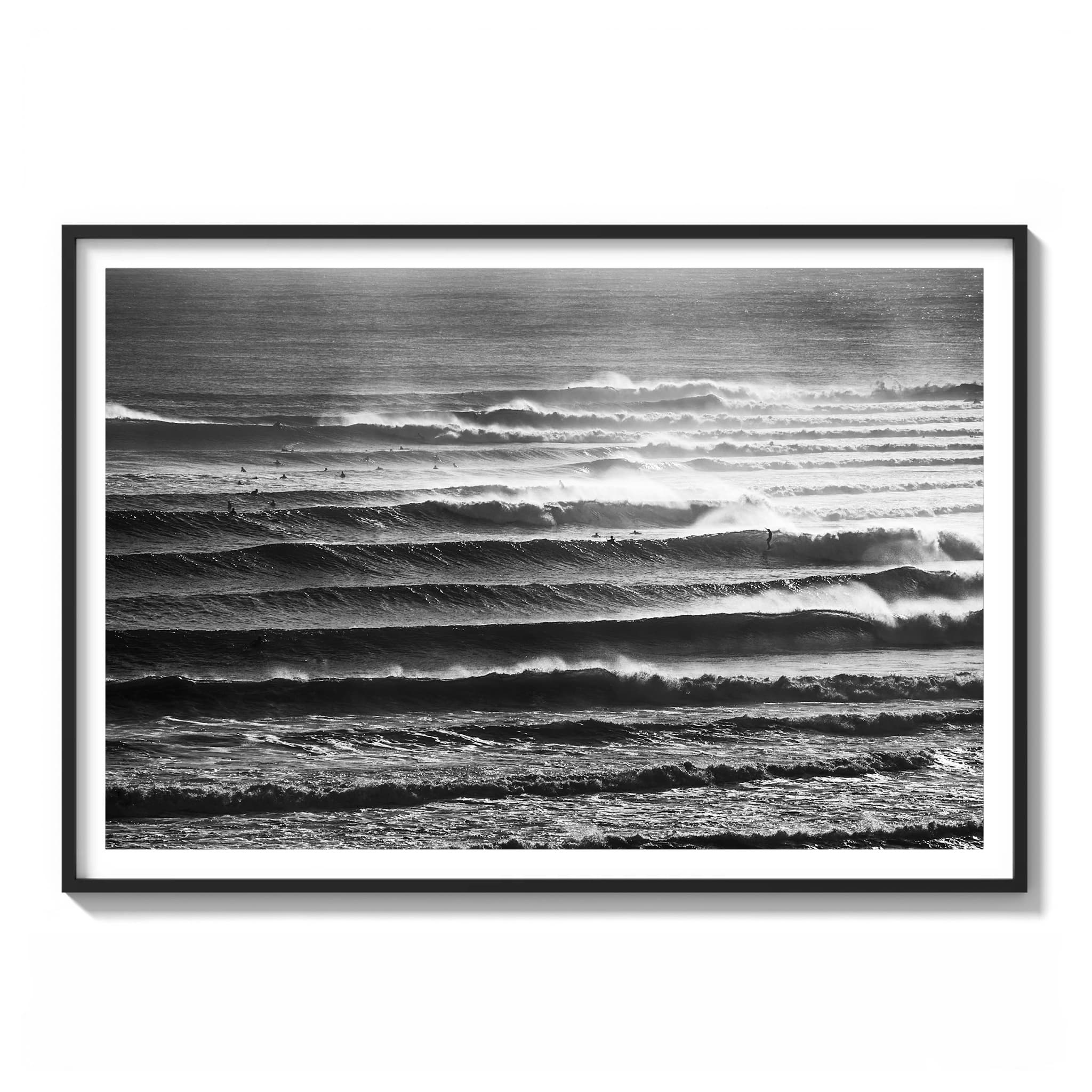 Black and white photograph of multiple parallel wave lines breaking along the Gold Coast with surfers scattered across the lineup framed.