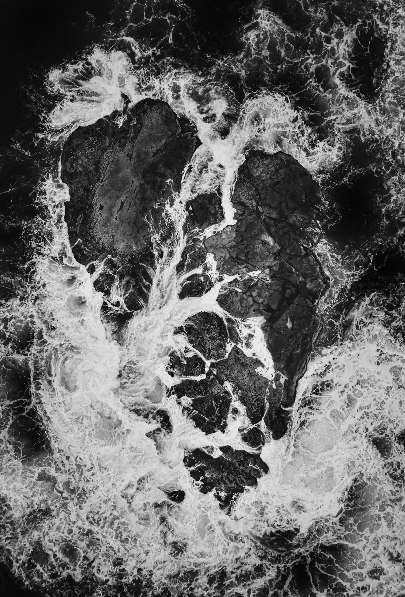 Aerial black and white photograph of a heart-shaped rock formation with white foam tracing through the cracks, Vancouver Island.
