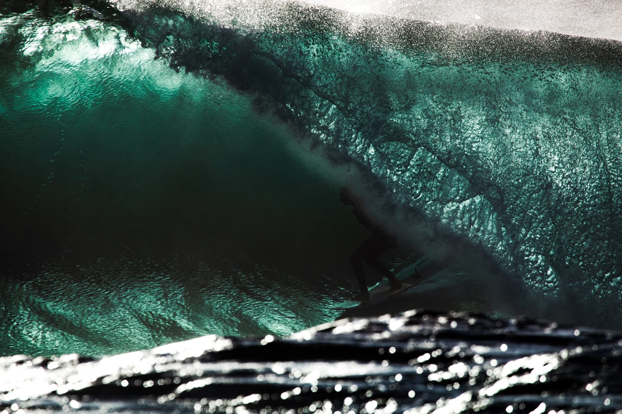 Color photograph of a surfer riding low inside a glassy green wave, sunlight fracturing through the barrel.