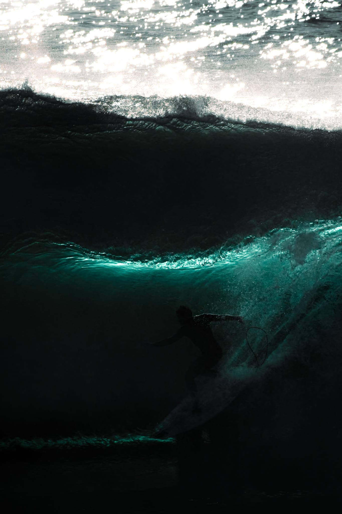Color photograph of a surfer riding in silhouette inside a dark wave with a thin ribbon of turquoise light, Sydney.