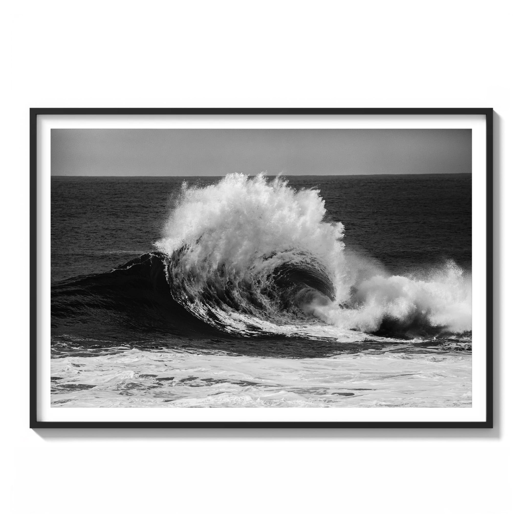 Black and white photograph of a large wave breaking at Cape Solander, spray flaring where backwash off the rock shelf collides with the incoming swell framed