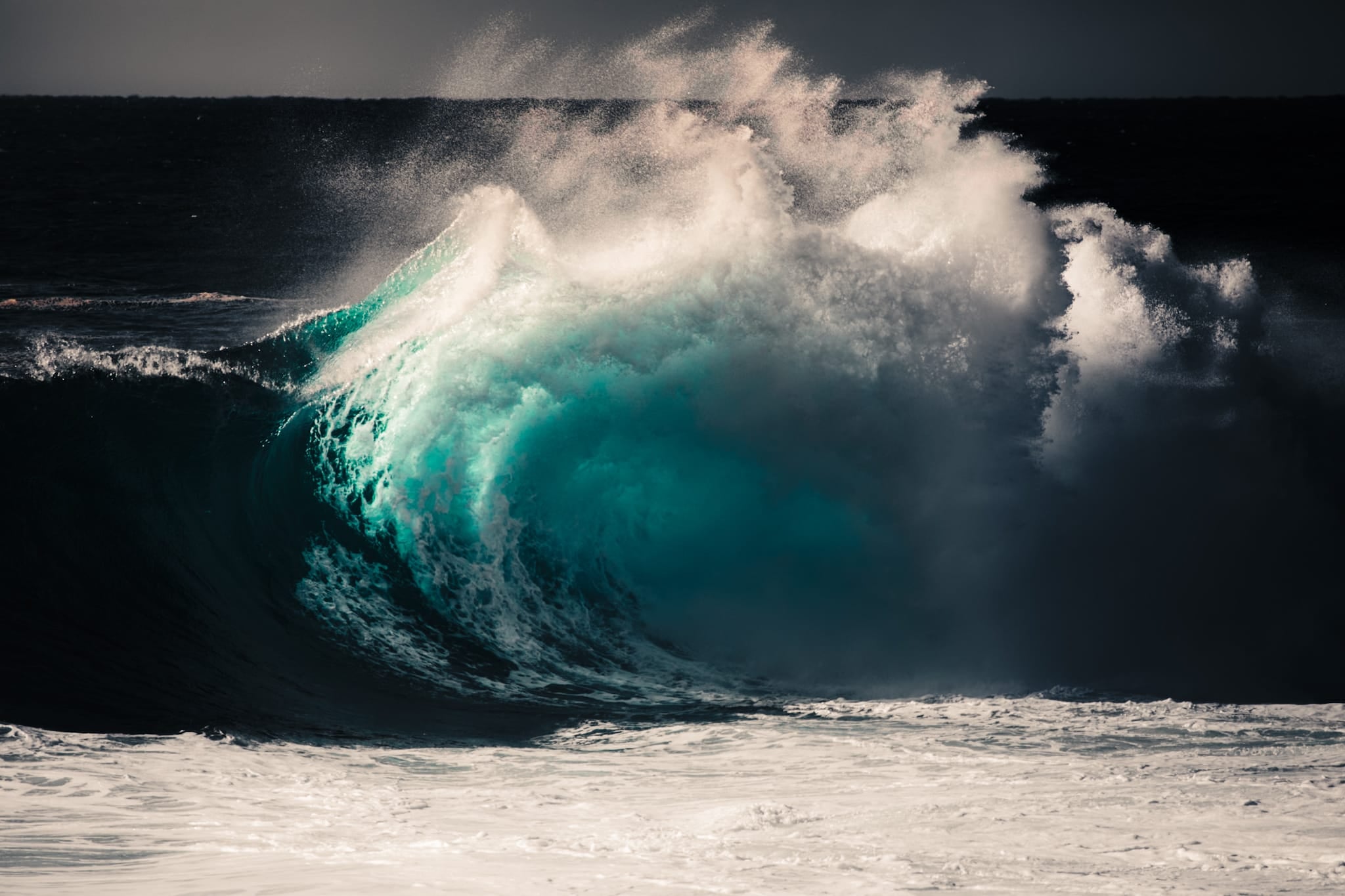 Color photograph of a glowing teal wave barrel breaking off the NSW coast of Australia against a dark sky.