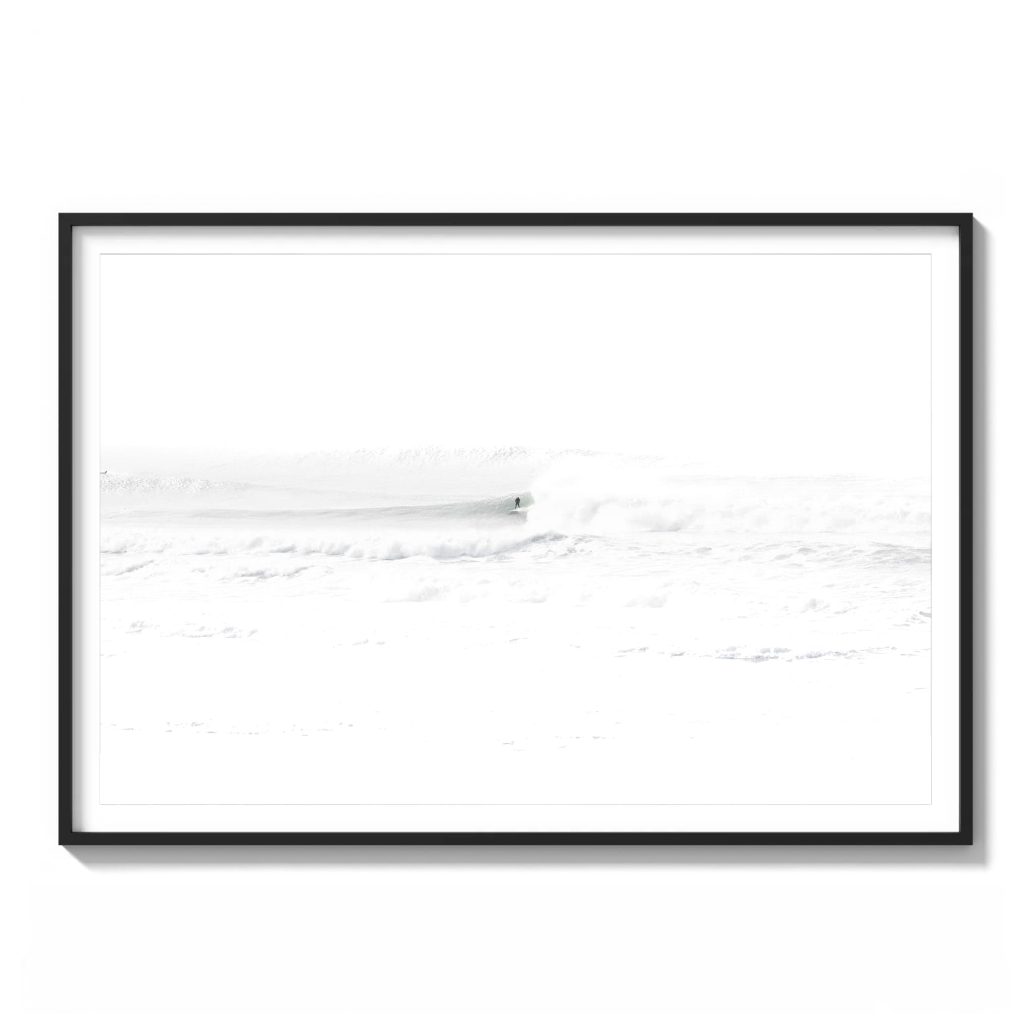 Framed high-key black and white photograph of a lone surfer riding a wave at Ocean Beach, San Francisco, nearly dissolved into white fog and spray.