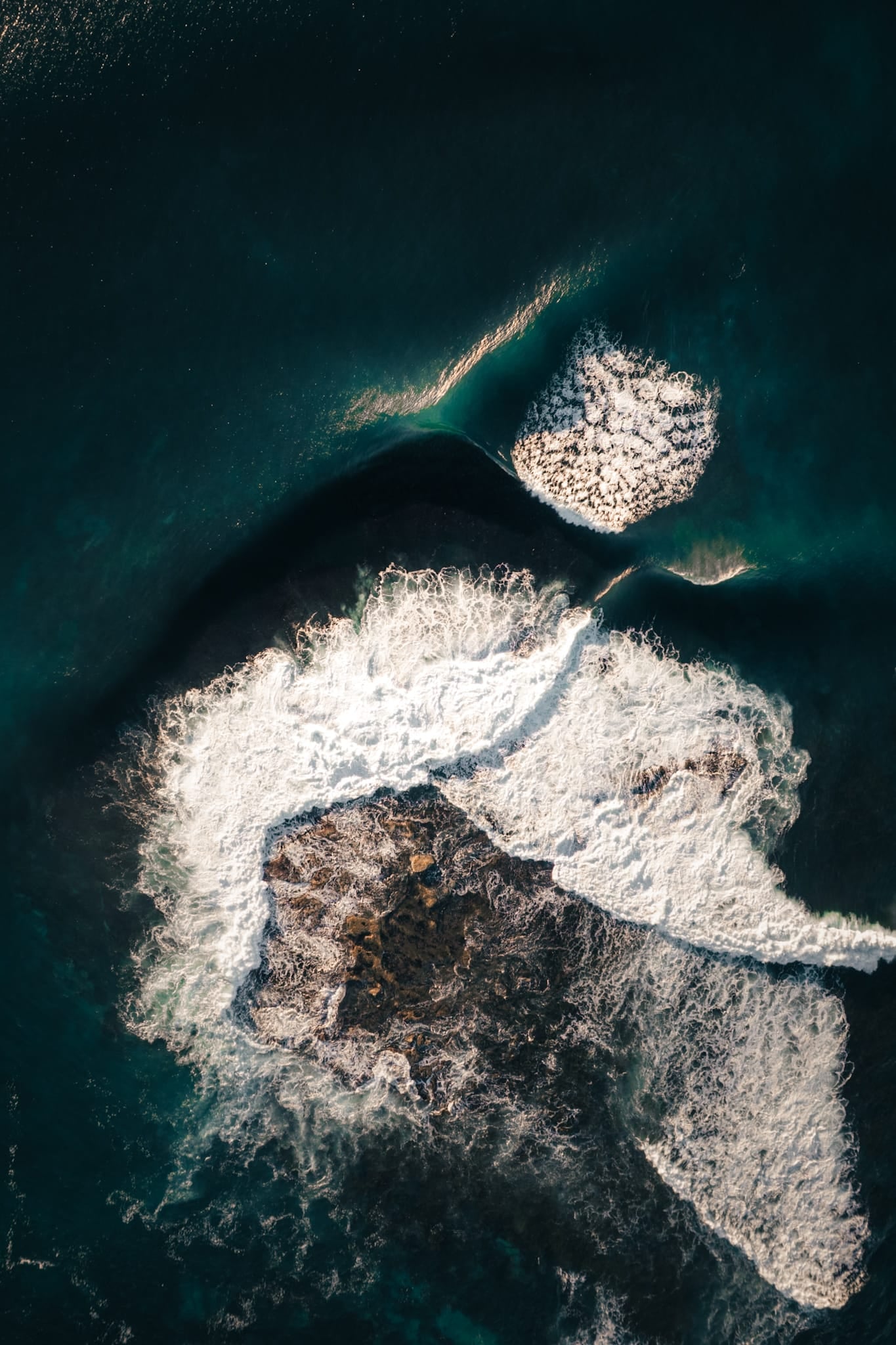 Aerial color photograph of dark rock and turquoise water with foam patterns at Shark Island, Sydney.