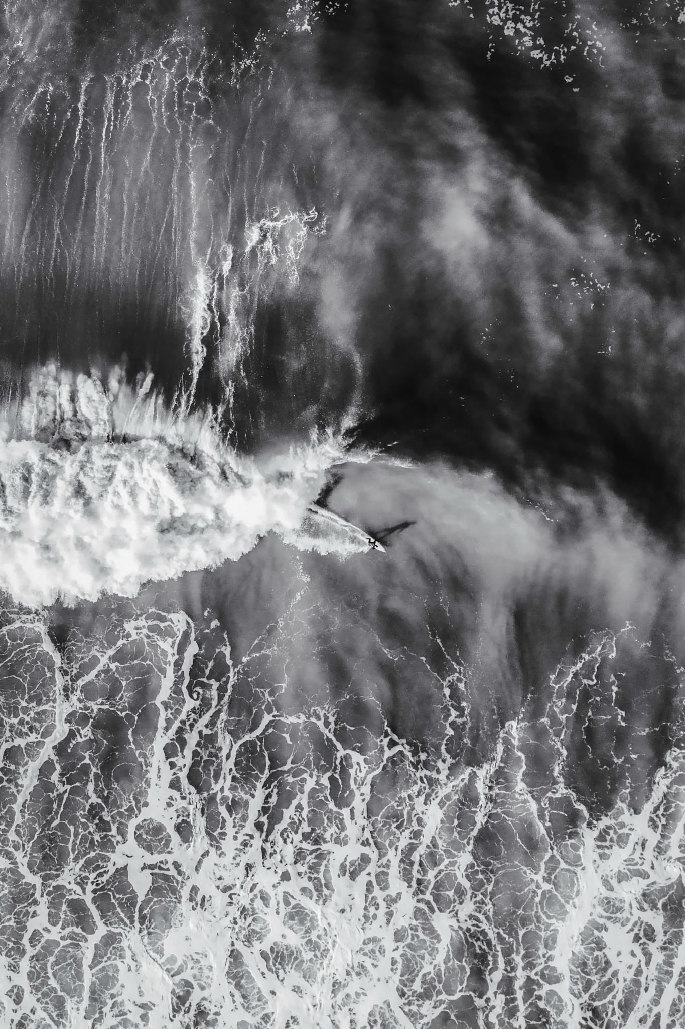 Aerial black and white photograph of a surfer riding a textured wave face at Ocean Beach, San Francisco.