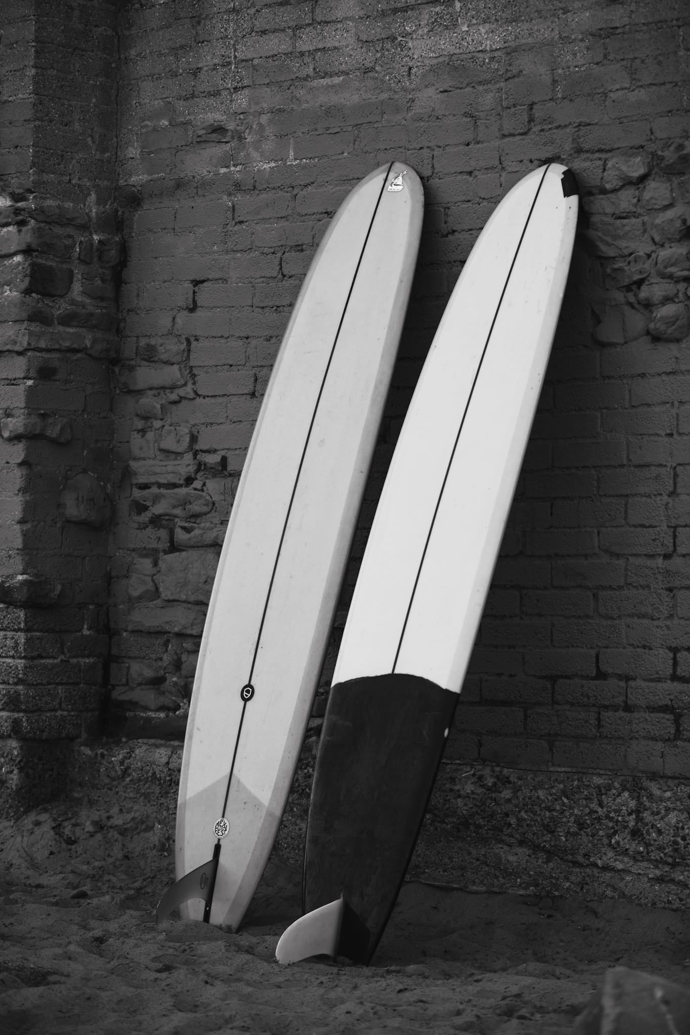 Black and white photograph of two longboards leaning against a brick wall in Malibu.