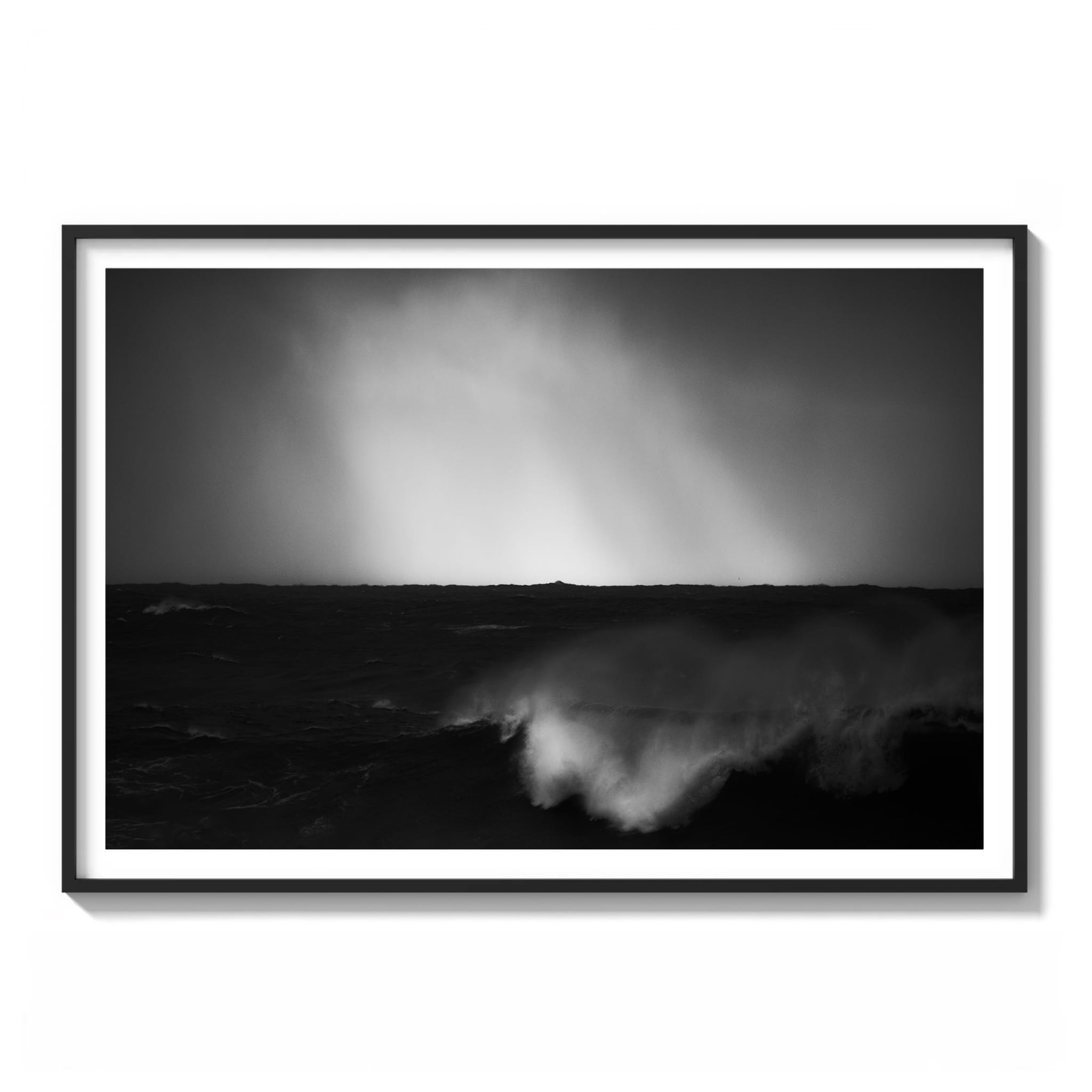 Framed black and white photograph of dramatic light rays breaking through clouds over a dark wave on the northern Sydney coastline.