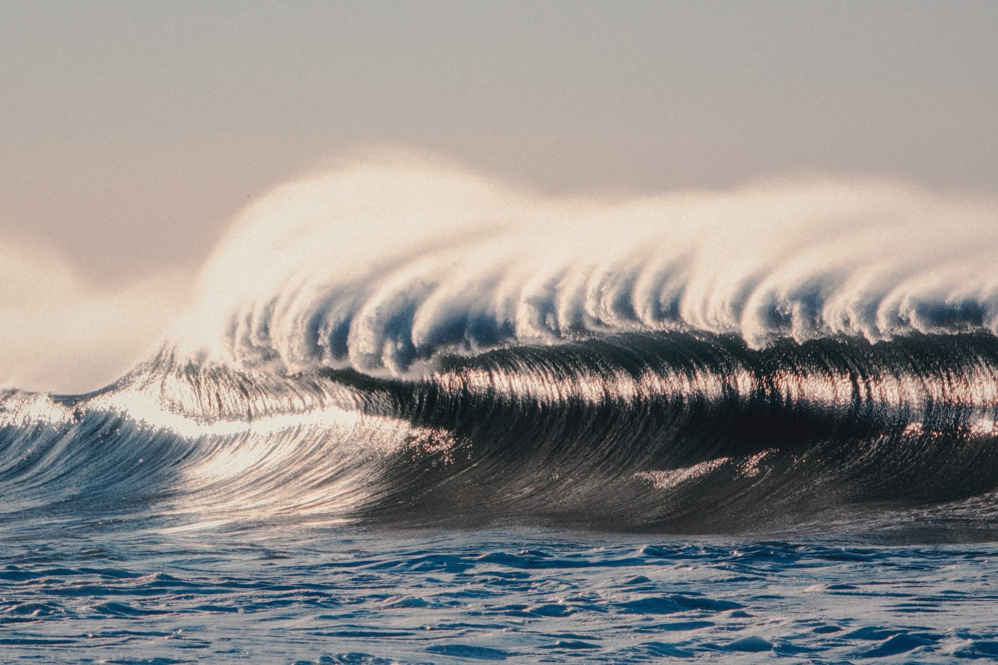 Warm sunrise photograph of a glassy, wind-groomed wave along the Malibu coastline with soft golden light.