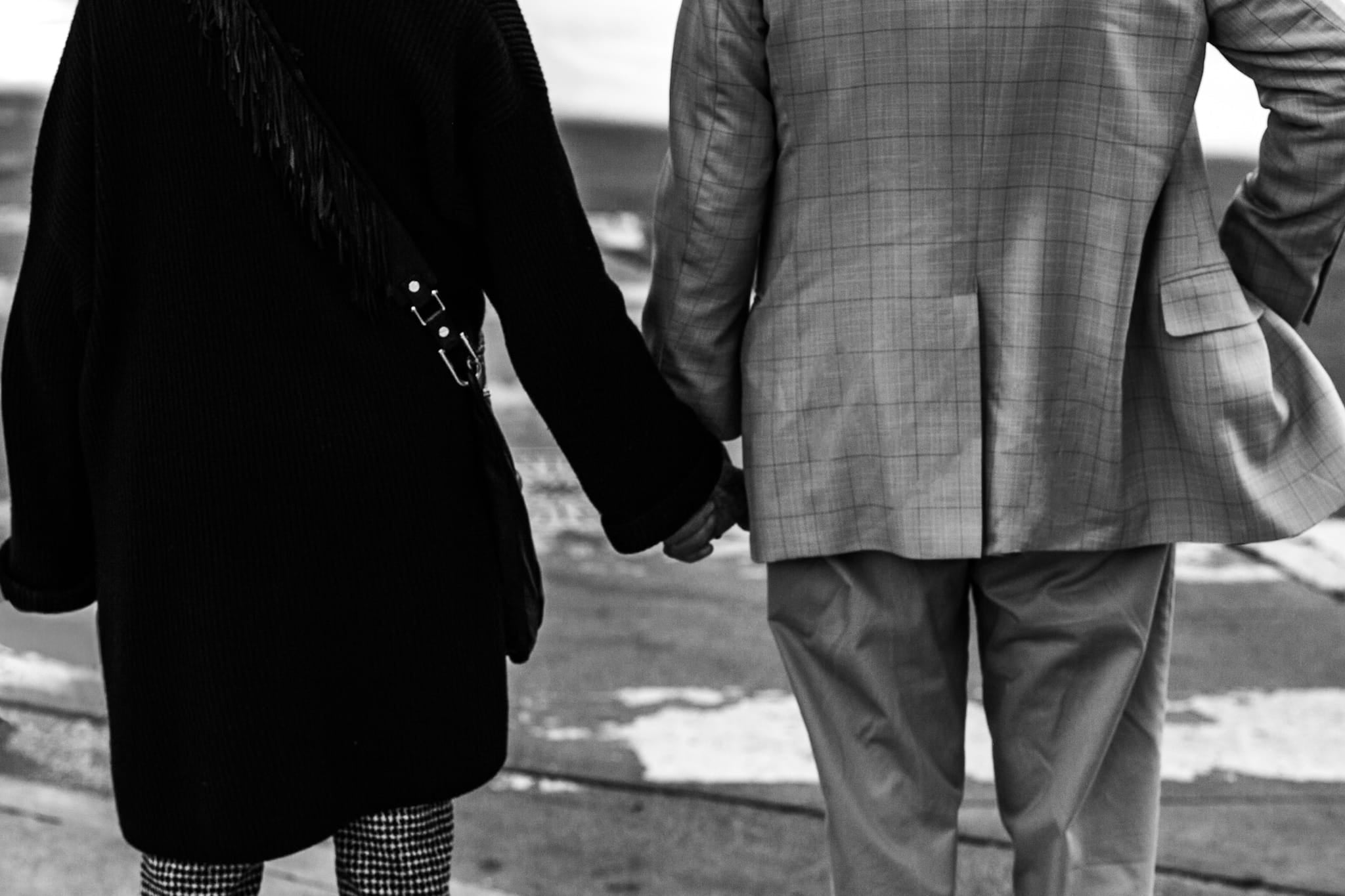 Black and white photograph of a couple holding hands from behind, looking out toward water in downtown Los Angeles.