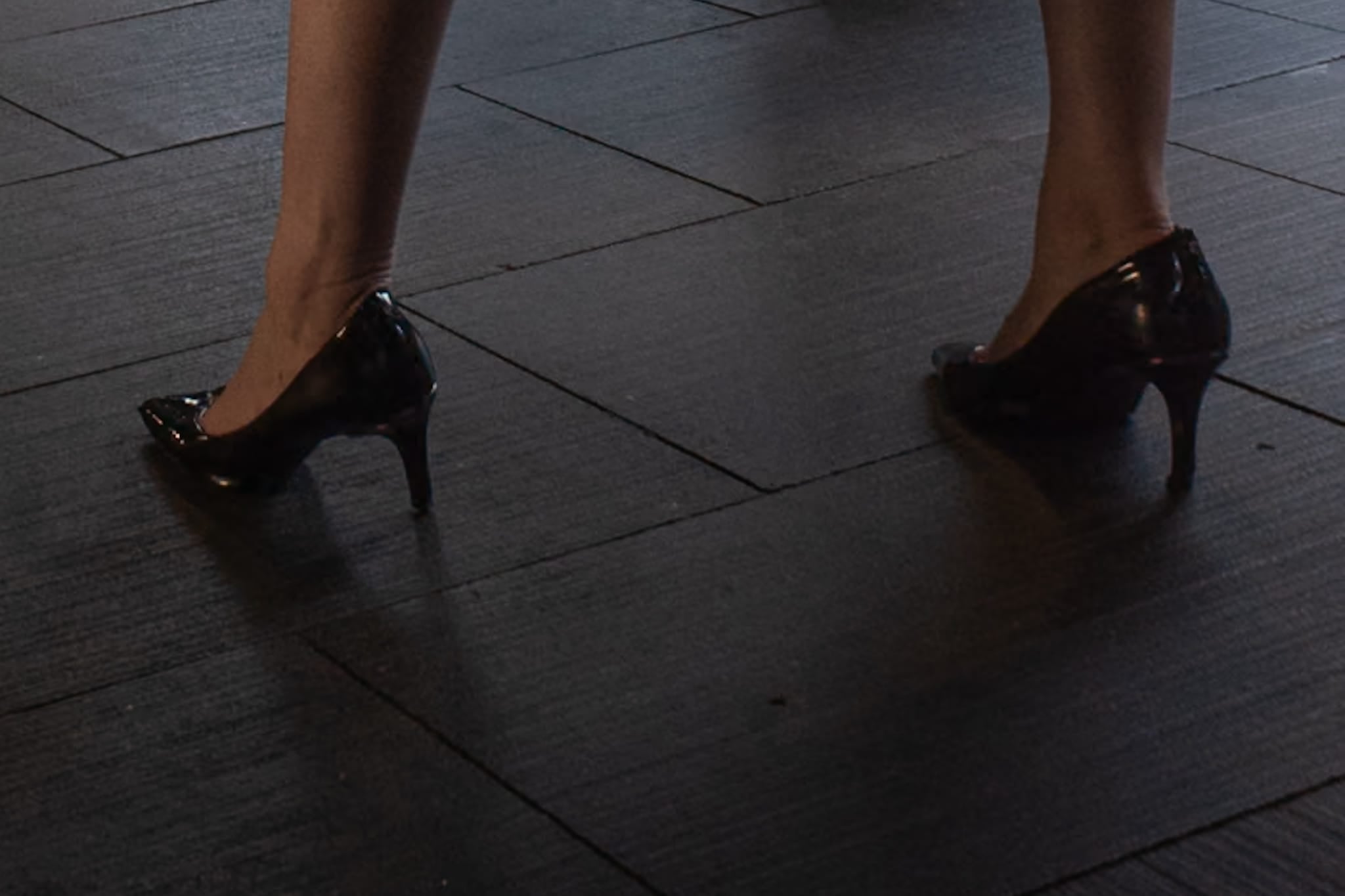 Color photograph of a person's feet in black heels walking on textured pavement in downtown Sydney.