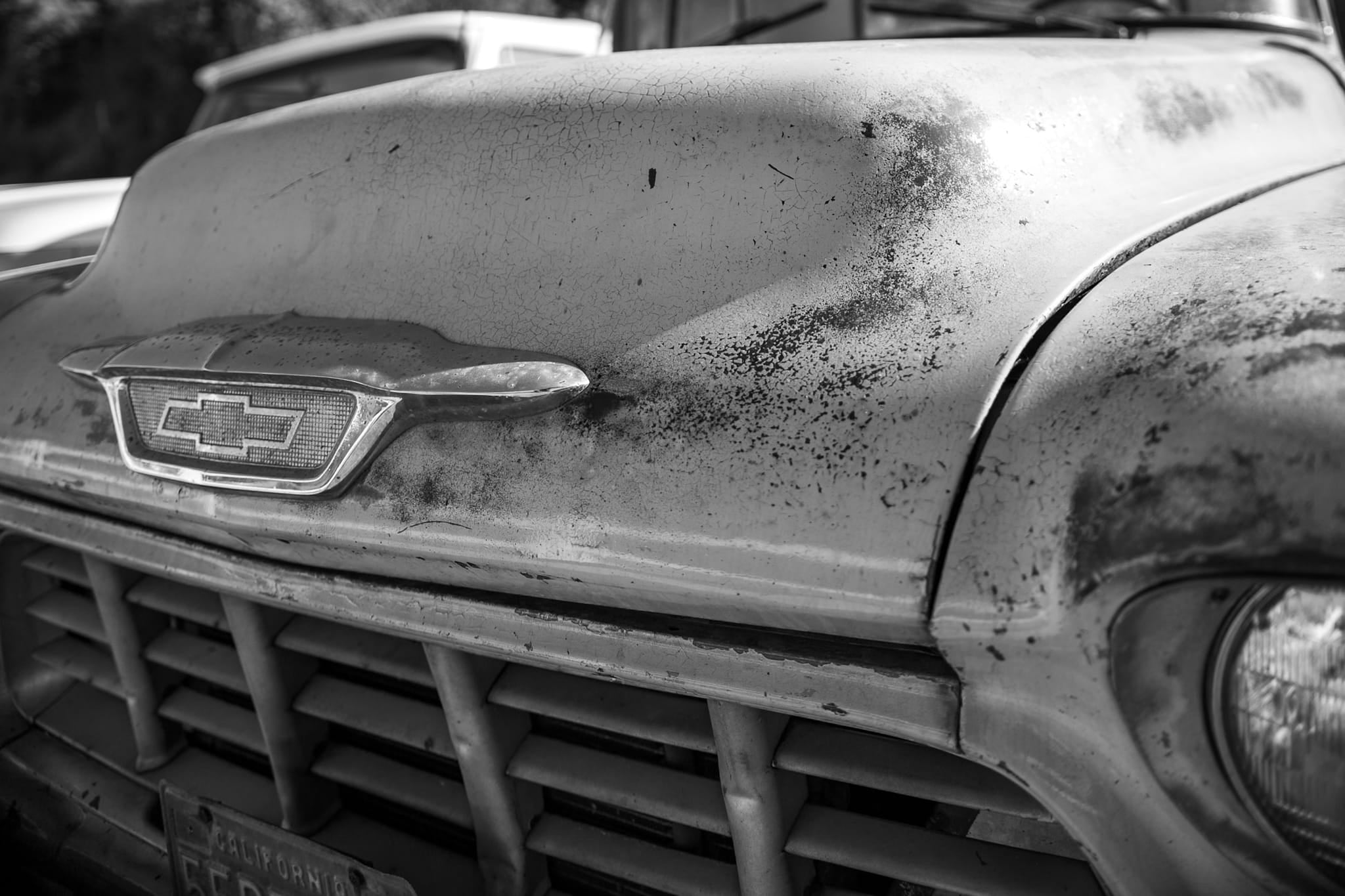 Black and white close-up photograph of a weathered vintage Chevrolet truck hood with cracked paint and rust patina in Los Angeles.