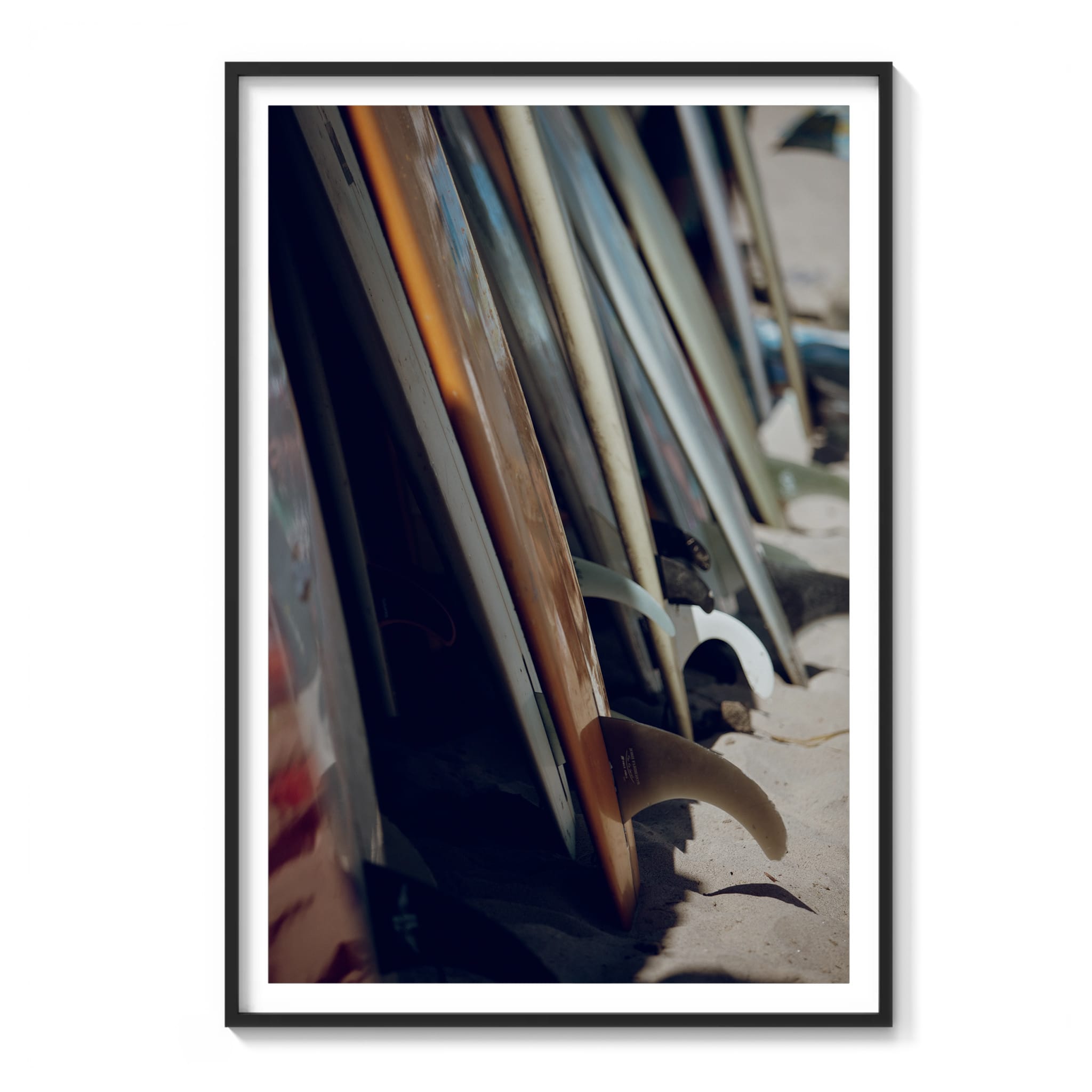 Framed color photograph of a row of surfboards leaning together on the sand in Malibu, one with a bright orange rail.